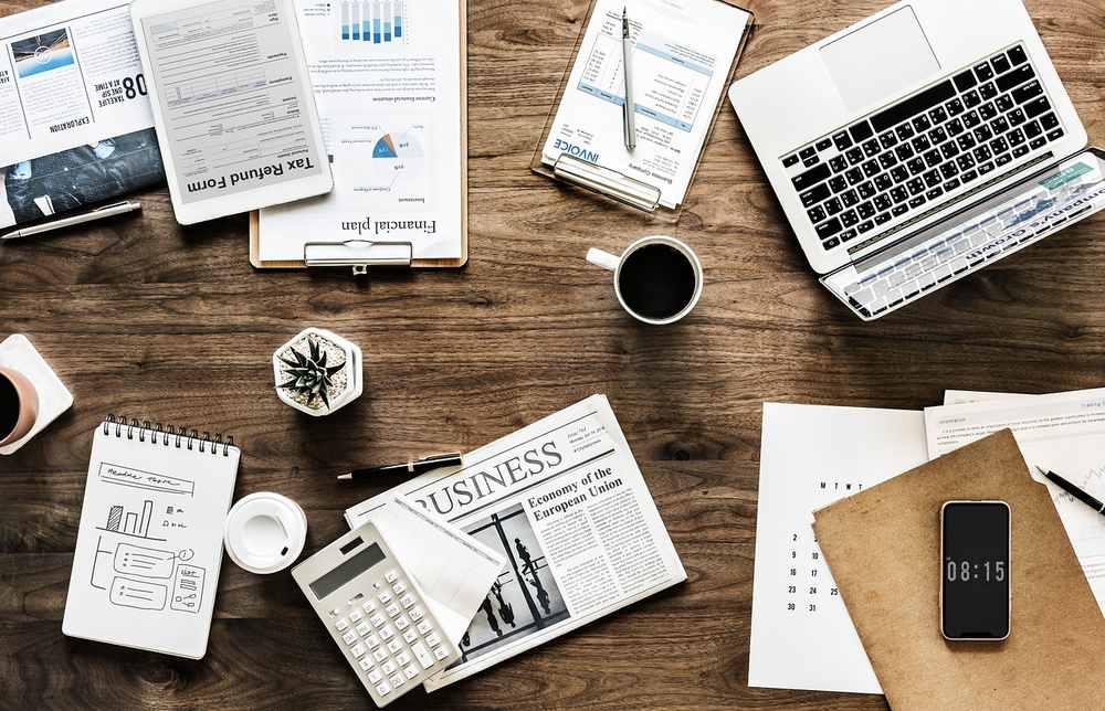 Bureau de travail avec ordinateur portable, documents éparpillés, journal, téléphone et café
