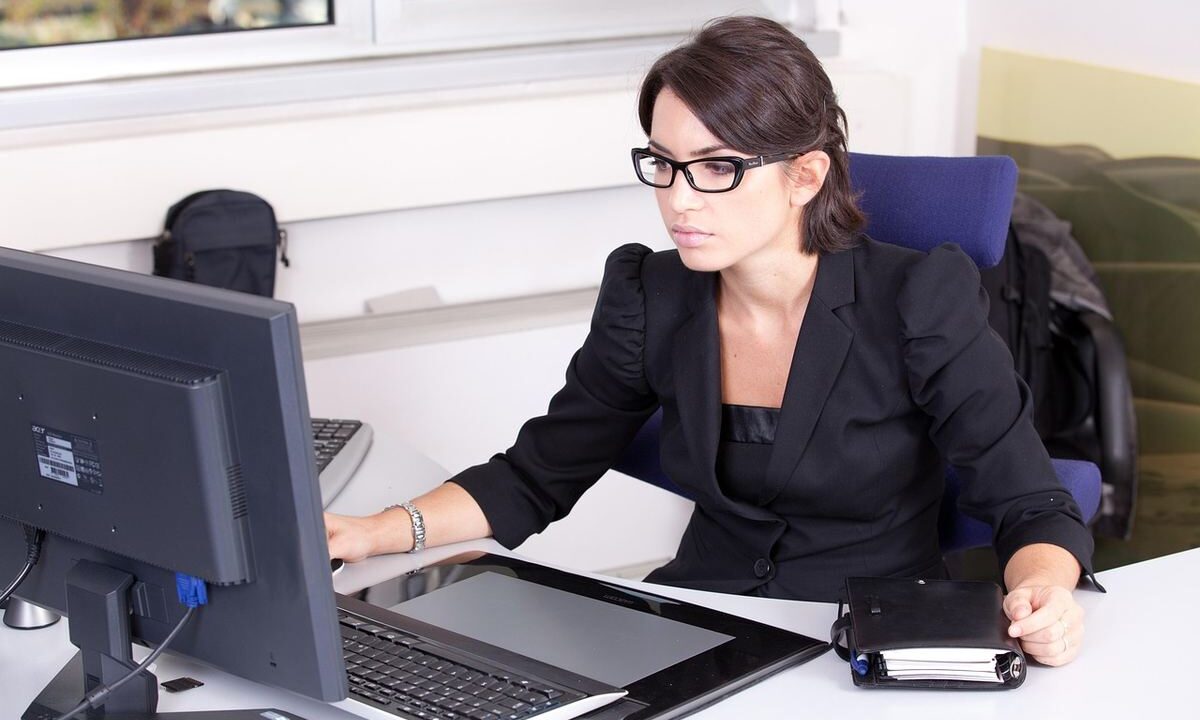 Une femme en costume noir travaille sur son ordinateur de bureau