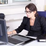 Une femme en costume noir travaille sur son ordinateur de bureau