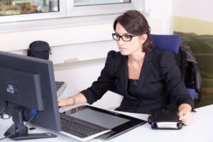 Une femme en costume noir travaille sur son ordinateur de bureau