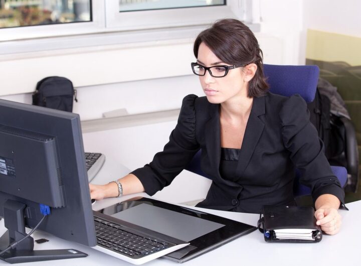 Une femme en costume noir travaille sur son ordinateur de bureau